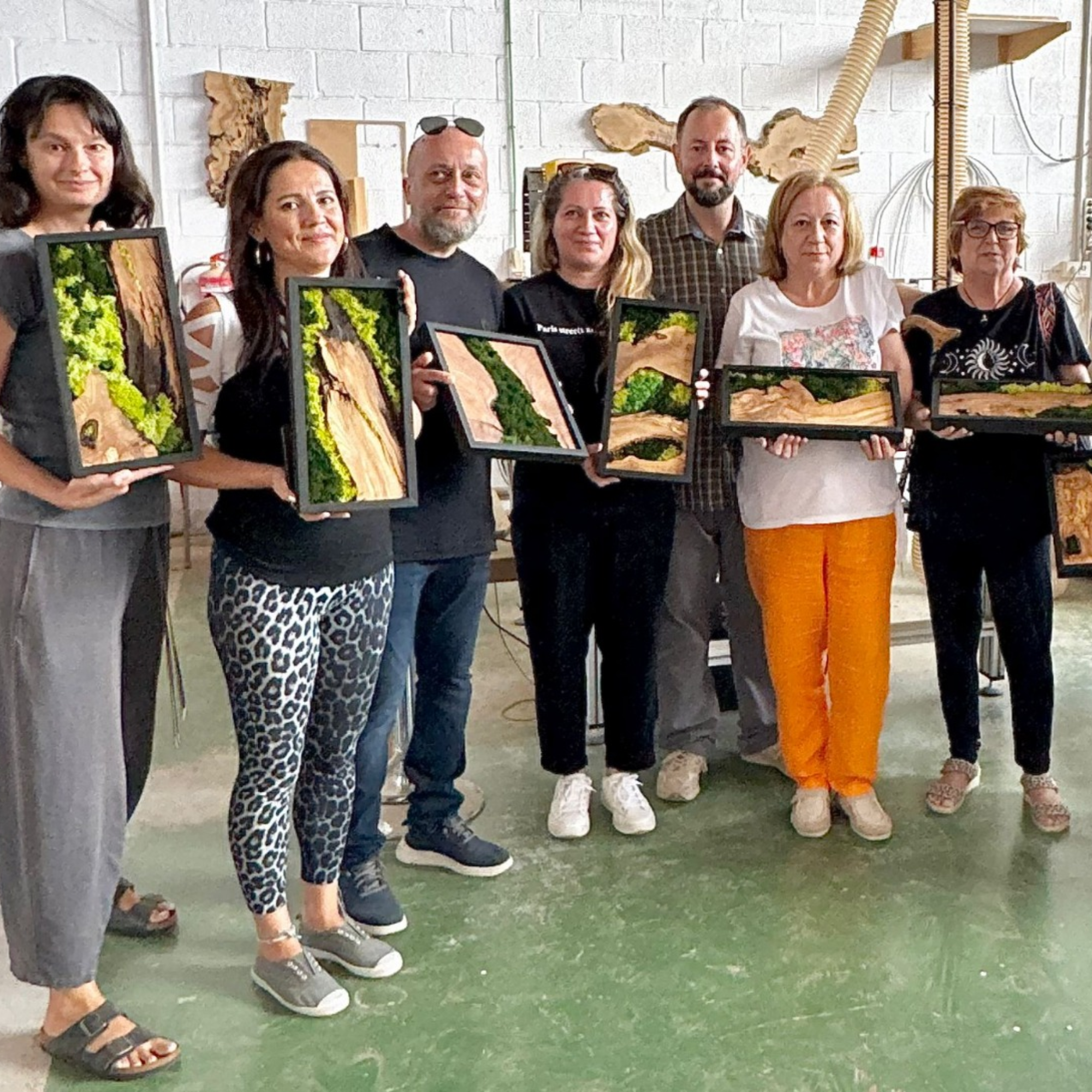 Group of people holding framed artworks in a workshop setting